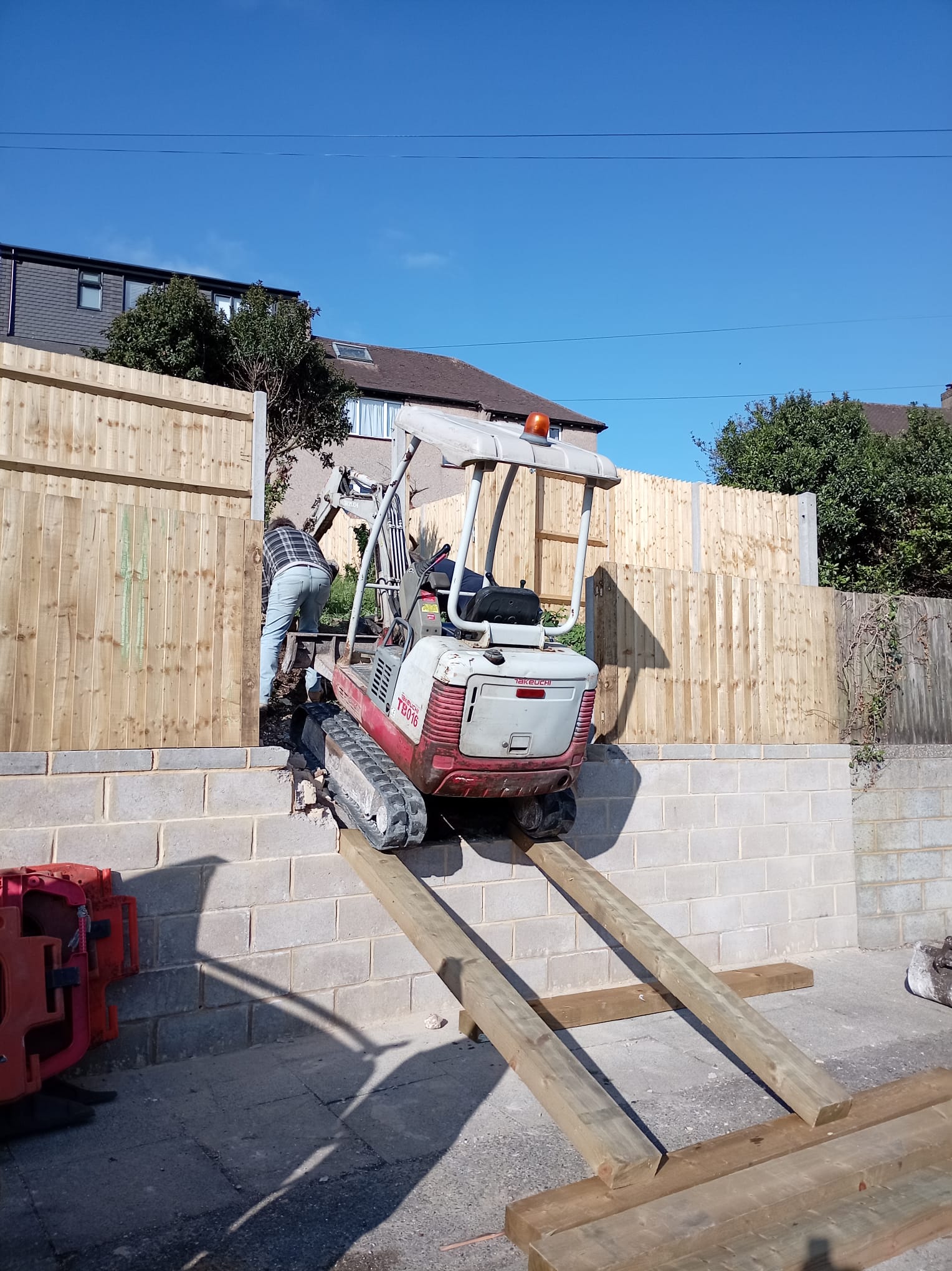 Mini digger driven up a timber access ramp on a groundworks job