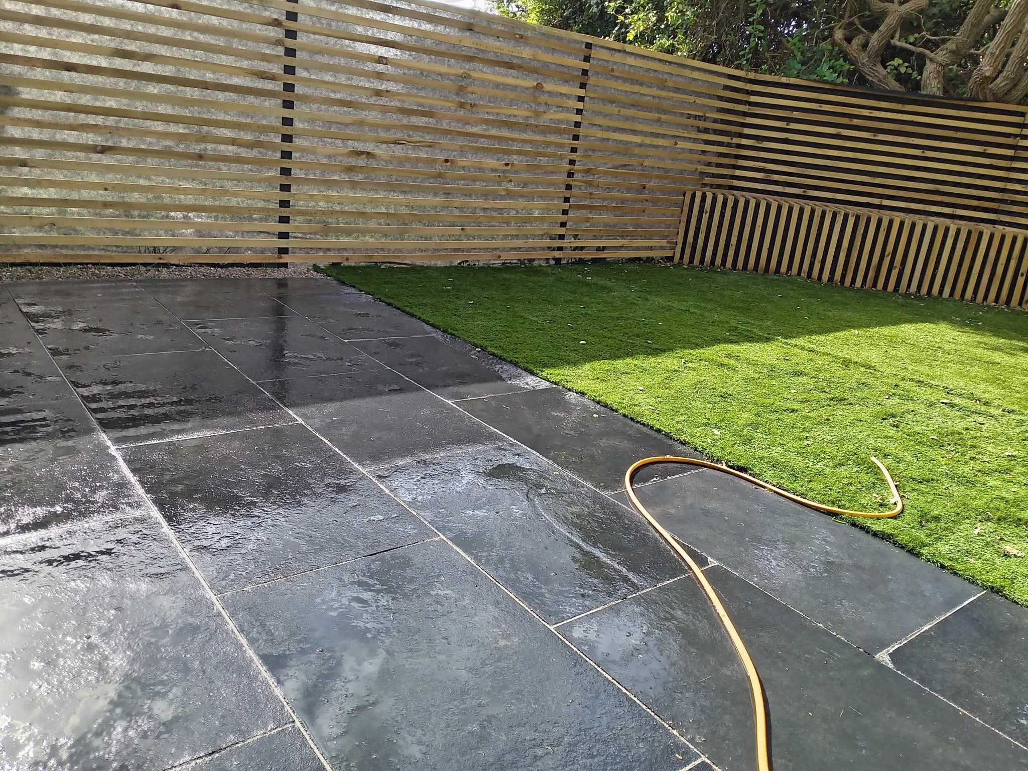 Slate paved patio alongside a new lawn and slatted fence